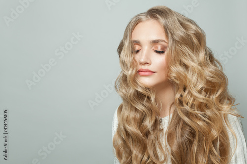 Attractive woman with long blonde healthy curly hair on white background
