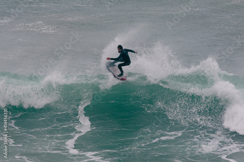 Surfer Carving and performing tricks on huge blue waves in Newquay, Cornwall - Southwest England