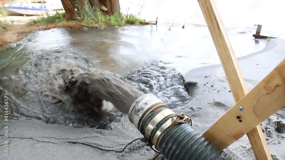 Close-up big pipe of power pump machine pouring mud sludge waste water with sand and silt on ground. Sand-wash and coast-depeening. Septic sewage maintenance service. spring flood deluge aftermath