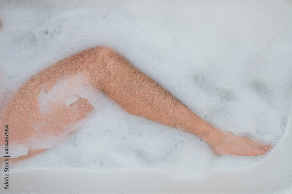 Funny picture of a man taking a relaxing bath. Close-up of male feet in a bubble bath. Top view