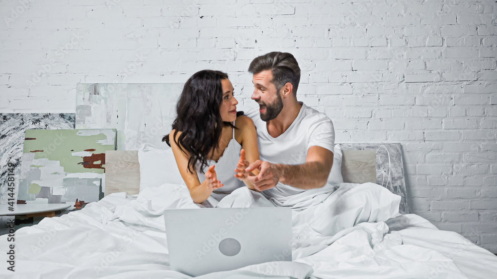 excited man pointing at laptop while watching movie with girlfriend in bedroom