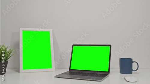 Two elecronic devices: laptop computer and tablet with green screen on a white office desk. Chroma key
