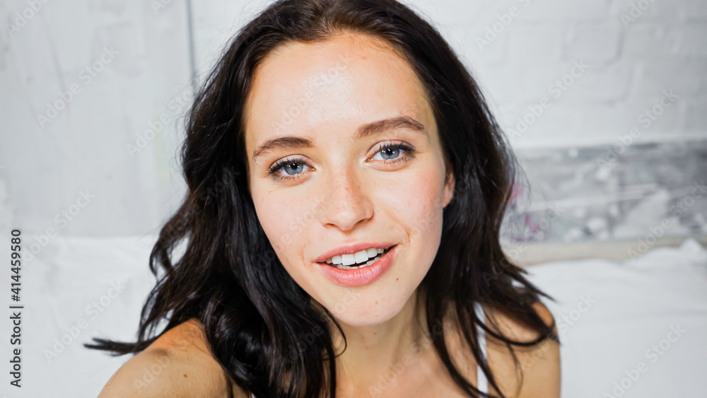 portrait of young brunette woman smiling at camera in bedroom portrait of young brunette woman smiling at camera in bedroom