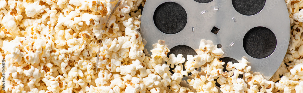 top view of film bobbin on airy delicious popcorn, banner, cinema concept