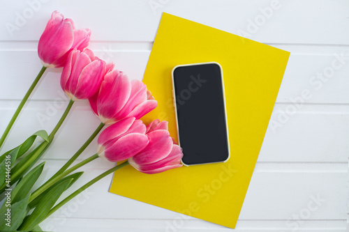 spring pink tulips, smartphone and yellow sheet of paper on a white background, top view, postcard