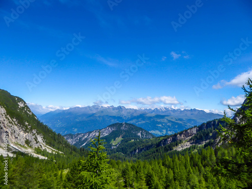 A beautiful panorama of Dolomites in Lienz, Austria. Mountain range is spreading endlessly. Few clouds above the peaks. Green trees and bushes overgrowing the slopes.