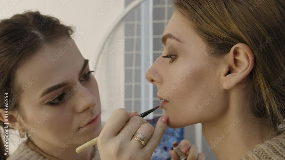 Make-up artist apply pink glitter on lipstick with brush on a womans lips Make-up artist apply pink glitter on lipstick with brush on a womans lips