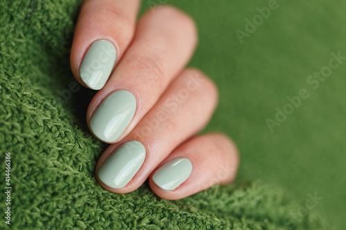 Female neat hand with short natural nails painted with mint nail polish holding knitted green fabrics. Natural, cozy, elegant, modern look.
