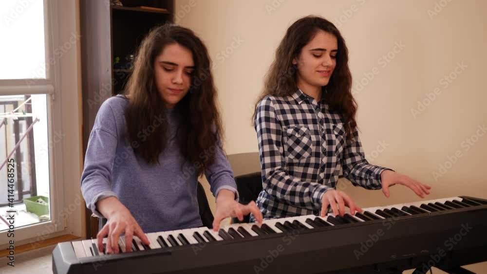 Teenage girls twin sisters at home play electronic piano in four hands during music rehearsal Teenage girls twin sisters at home play electronic piano in four hands during music rehearsal