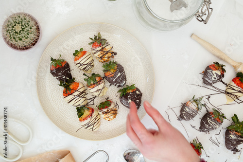 Homemade Chocolate strawberries with almonds on an off white plate and table. Human hand taking.
