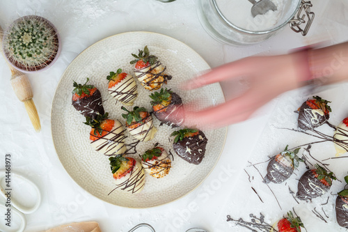 Homemade Chocolate strawberries with almonds on an off white plate and table. Human hand taking.
