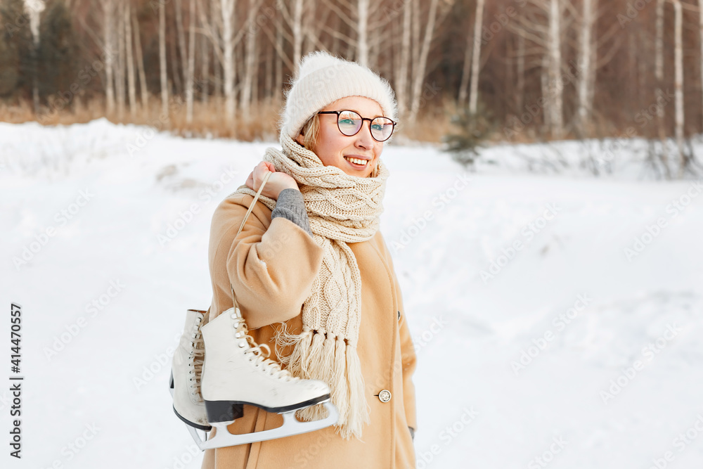 Fototapeta premium young woman in Park near the ice skating rink. girl in beige coat and hat is going to skate, winter leisure and relaxation