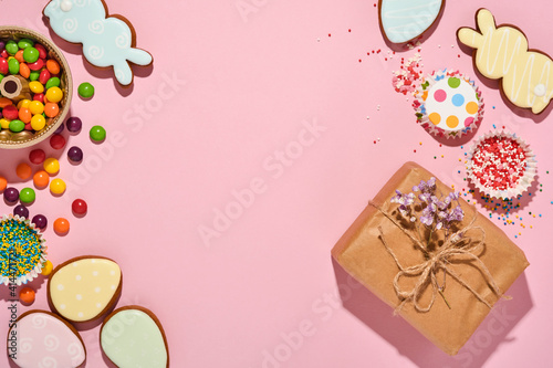 Easter baking background. Easter multicolored gingerbread, candy, scattered confectionery topping dressing and gift box on pink background. Celebratory background concept. Space for text.