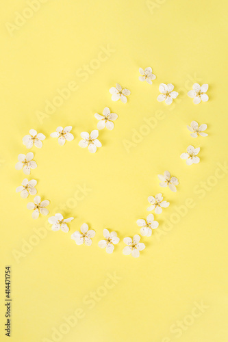 Heart of spring or summer flowers on a yellow background. Flowers composition. Copy space for your text. Flat lay style. Top view.
