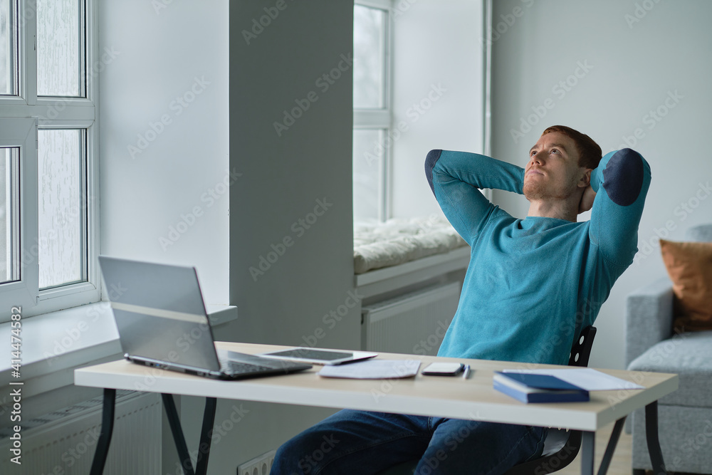Satisfied with work done. Man working from home happily surprised looking at a laptop with his hands on his head sitting on a sofa in living room with warm atmosphere. Satisfied with work done. Man working from home happily surprised looking at a laptop with his hands on his head sitting on a sofa in living room with warm atmosphere.