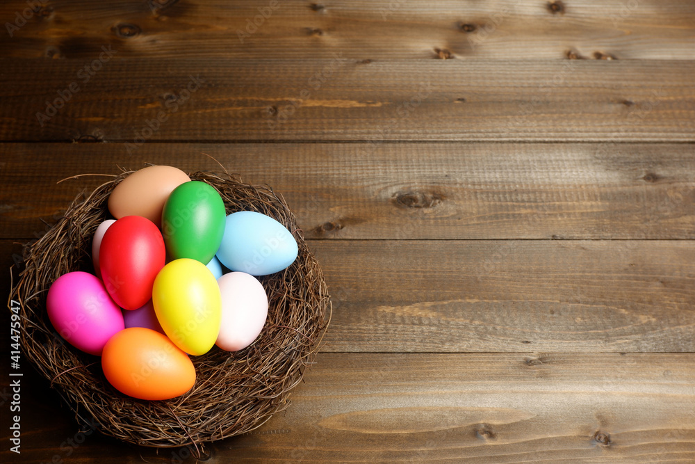 Multi colored easter eggs in birds nest on dark wooden planks table with copy space. Easter holiday banner, card, poster, voucher, header, invitation template Multi colored easter eggs in birds nest on dark wooden planks table with copy space. Easter holiday banner, card, poster, voucher, header, invitation template