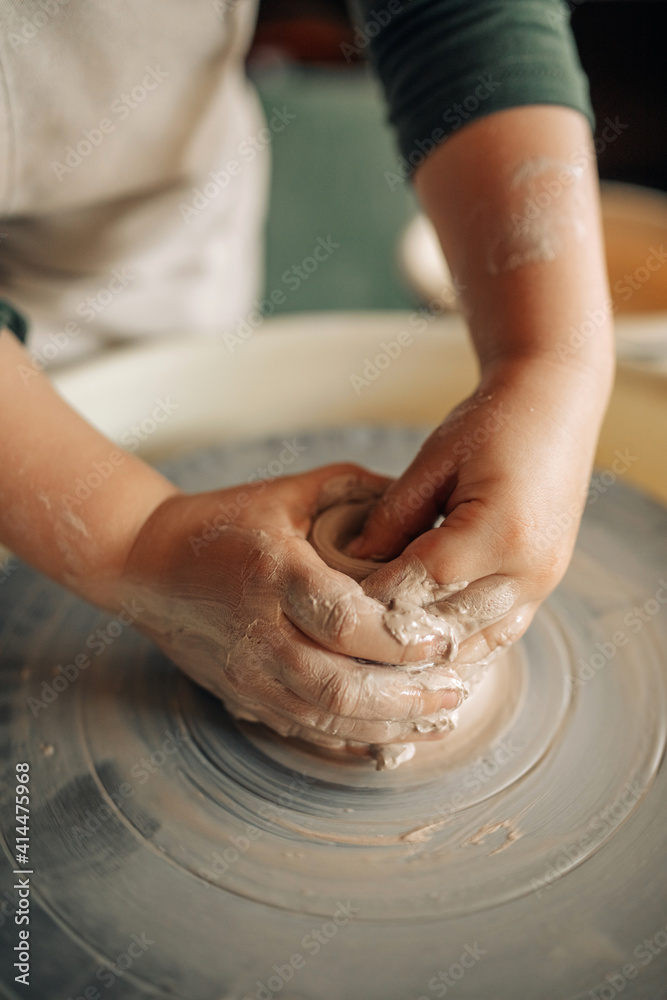 Child hands make earthenware cup on pottery wheel.