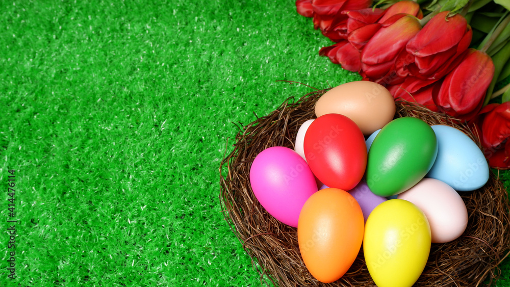 Multi colored easter eggs in birds nest and bouquet of red tulip flowers on green grass lawn background closeup view selective focus with copy space. Easter holiday banner, header  template