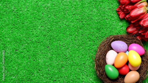 Multi colored easter eggs in birds nest and bouquet of red tulip flowers on green grass lawn background top view with copy space. Easter holiday banner, card, poster, voucher, header template