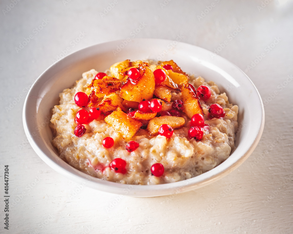 Oatmeal with caramelized apples and red currants in a white deep plate Oatmeal with caramelized apples and red currants in a white deep plate