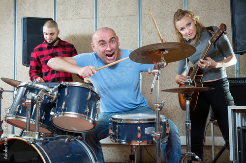 Group of young musicians with expressive male drummer practicing in rehearsal room