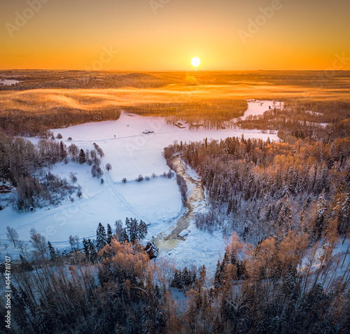 Warm sunrise over snowy countryside landscape. Pine forest covered in fog waves. Drone aerial view.