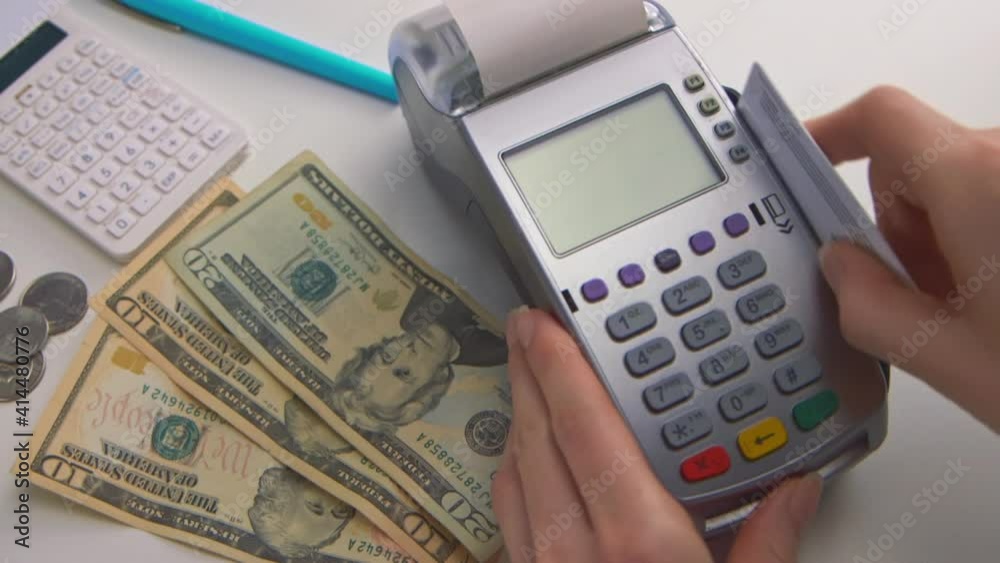 A woman's hand swipes a card into a debit machine. The screen says A woman's hand swipes a card into a debit machine. The screen says