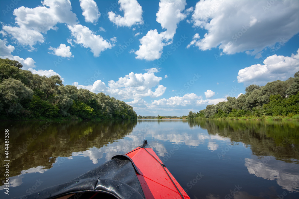 Summer kayaking on a river. Floating along big and calm river with fluffy clouds in the sky