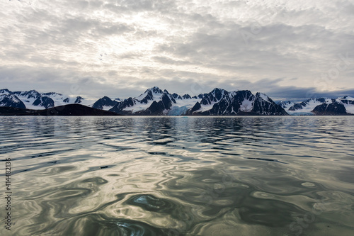 View of Raudfjorden in Svalbard with the snow-capped mountains at the horizon and the light reflecting off the ocean in the foreground.