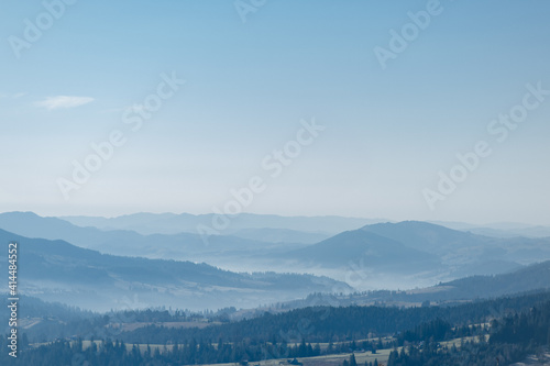 landscape of mountains in early spring with growing fir trees, dry grass and blue sky