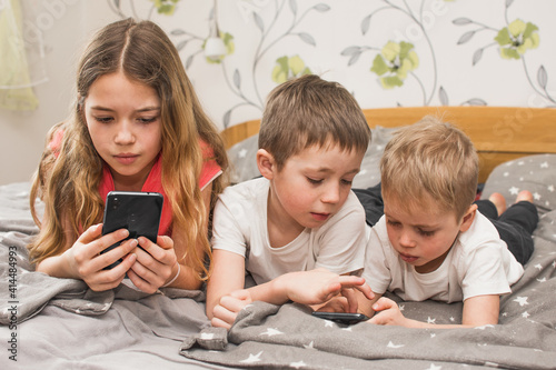 Wallpaper Mural Three children lying on bed at home and typing message on mobile phone. Technology and internet and social media in everyday life. Torontodigital.ca