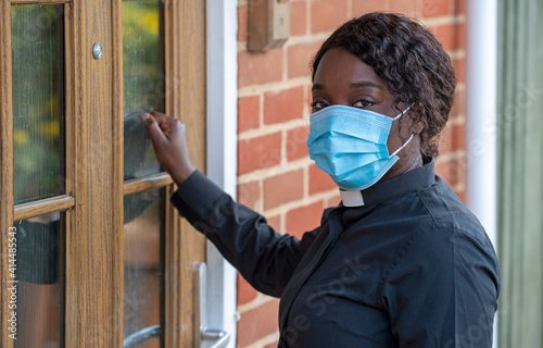 England, UK, December 2020. A black minister wearing a protective medical mask and white collar during Coronavirus outbreak. Making a house call.
