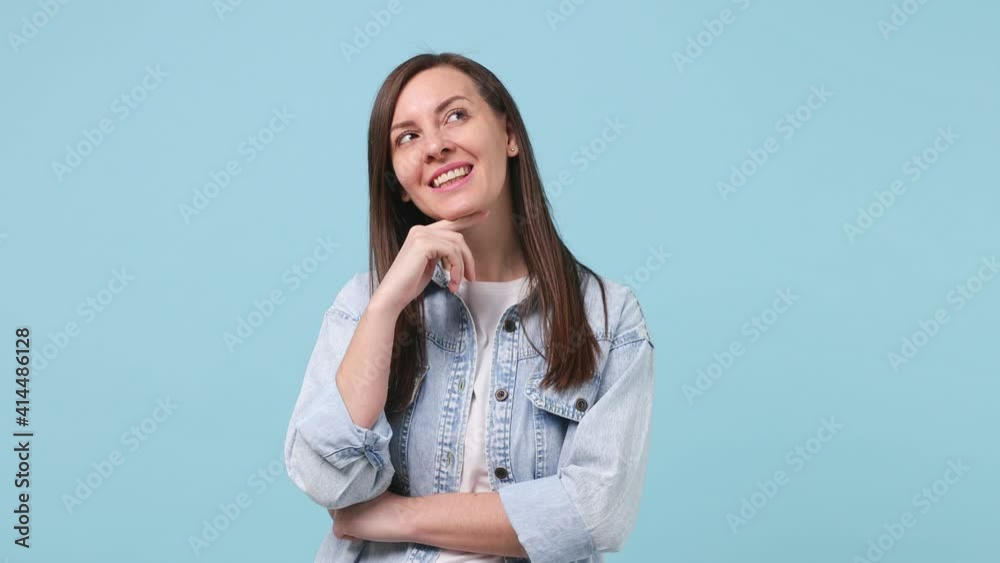 Smiling beautiful long hair young woman 30s years old in denim jacket white t-shirt look around think dream put hand prop up on chin isolated on pastel blue background studio. People lifestyle concept Smiling beautiful long hair young woman 30s years old in denim jacket white t-shirt look around think dream put hand prop up on chin isolated on pastel blue background studio. People lifestyle concept