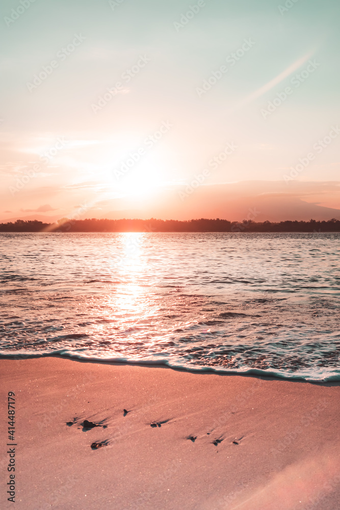 Beautiful orange and teal sunrise over the ocean as the beach sand sparkles in the sun in Gili Trawangan, Lombok, Indonesia.
