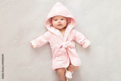 Baby girl in a Terry robe and diaper after bathing. Kid in a hood. Cute happy laughing baby girl in pink soft robe after bath. Baby in a clean and dry towel.