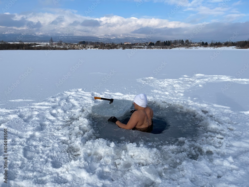 Naklejka premium hardy man in ice water with snow with white cap