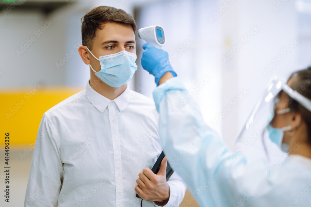 Temperature screening office workers. Disease control expert in visor and protective gloves with an Infrared thermometer equipment to check the temperature at office during pandemic in quarantine. Temperature screening office workers. Disease control expert in visor and protective gloves with an Infrared thermometer equipment to check the temperature at office during pandemic in quarantine.