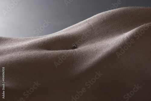 Closeup of the abdomen of a sexy naked woman against a gray background