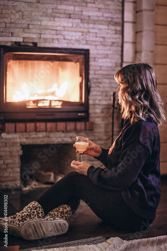 woman sitting by the fireplace with a glass of wine in her hands