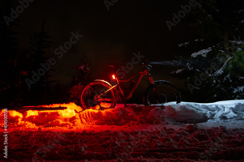 Bicycle in the night in a snowy winter landscape with red and white light, in nature