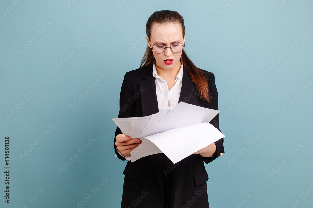 Business woman looks through documents standing on a blue background. Office workdays of an office worker Business woman looks through documents standing on a blue background. Office workdays of an office worker