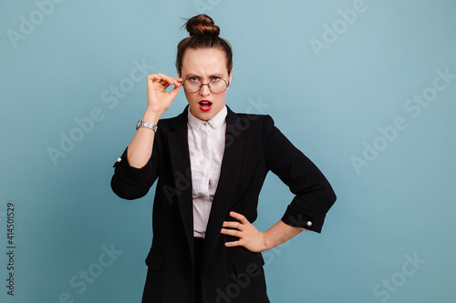 Outraged office worker holding on to glasses on a blue background! Indignation and indignation of workers and businessmen. The girl's indignant face