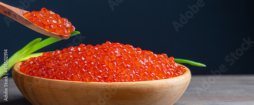 Red caviar in a wooden cup on a wooden background with a spoon.