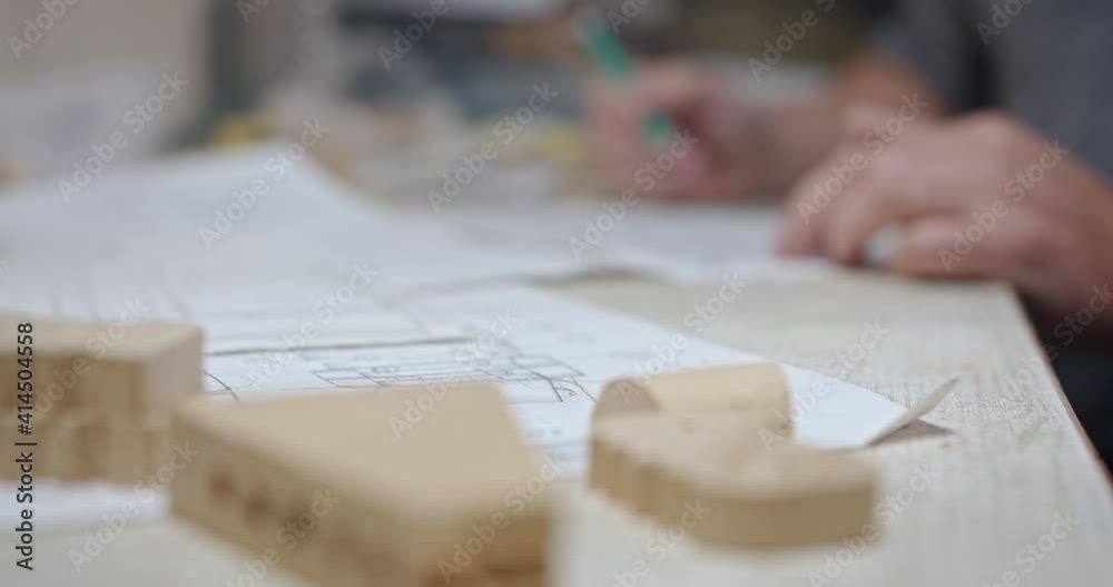 Artisan man drawing scheme of woodwork in workshop. Side view of crop anonymous skilled craftsman with pencil making sketch on paper while working at table with shaped wooden details in workshop Artisan man drawing scheme of woodwork in workshop. Side view of crop anonymous skilled craftsman with pencil making sketch on paper while working at table with shaped wooden details in workshop