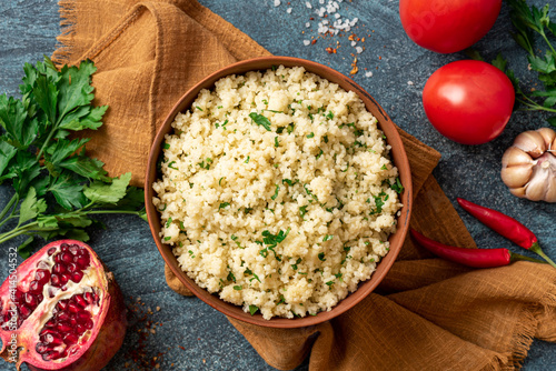 Cooked couscous with parsley in a ceramic bowl on a dark background top view. Maghreb cuisine, vegan food.  photo