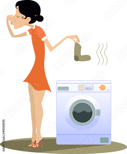 Woman is going to wash dirty laundry in the washing machine. Young woman stands near washing machine holds her nose from dirty laundry odor nuisance isolated on white
