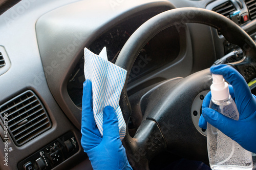 The driver in blue rubber gloves washes the steering wheel of the car with a rag and sanitizer