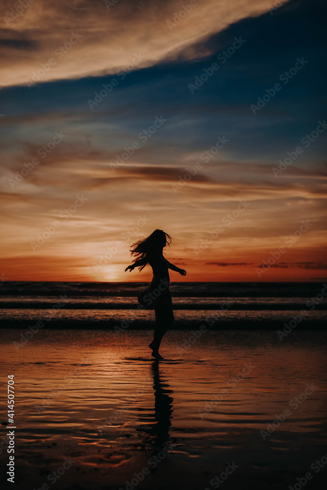 Woman enjoying sunset at the beach. Golden hour sunset. Sunset seascape. Bright sunlight. Ocean with waves. Island Bali, Indonesia