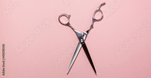 Flat lay of professional hair cutting shears in the centre of the frame on bright pink background. Hairdresser salon equipment concept with copy space