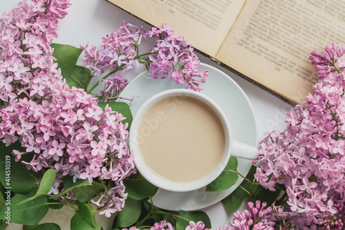 spring composition flat lay white cup of coffee, pink lilac beautiful bouquet of lilacs, old book, concept of spring and comfort 